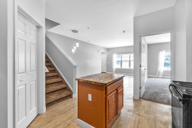 kitchen featuring a kitchen island, black electric range, hanging light fixtures, and light wood-type flooring