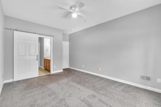 unfurnished bedroom featuring a barn door, ceiling fan, connected bathroom, and light carpet