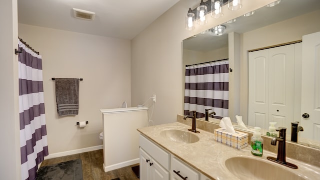 bathroom featuring double vanity, toilet, wood finished floors, and a sink