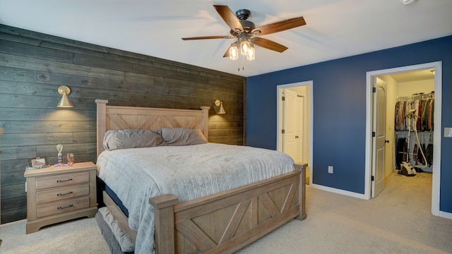 bedroom featuring a walk in closet, light carpet, a ceiling fan, a closet, and baseboards