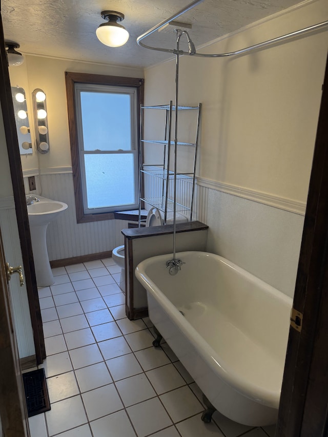 bathroom with a textured ceiling, tile patterned floors, a tub, and toilet