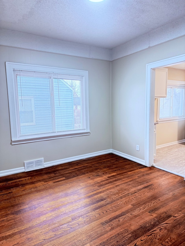 spare room featuring dark hardwood / wood-style floors, a textured ceiling, and a wealth of natural light