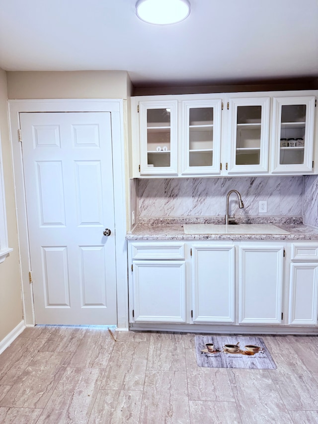 kitchen featuring sink, white cabinets, light stone counters, and decorative backsplash