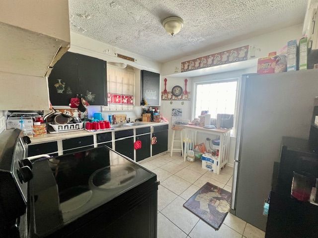 kitchen with stainless steel refrigerator, sink, a textured ceiling, and light tile patterned floors