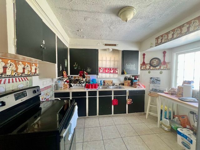 kitchen featuring electric stove, sink, a textured ceiling, and light tile patterned floors