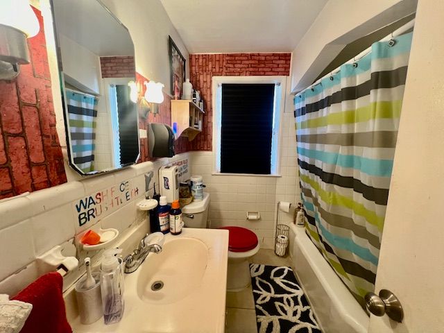 full bathroom featuring toilet, sink, tile walls, shower / bathtub combination with curtain, and tile patterned flooring