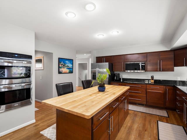 kitchen featuring butcher block counters, dark brown cabinets, light hardwood / wood-style flooring, a kitchen island, and stainless steel appliances