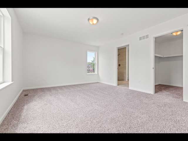 unfurnished bedroom featuring connected bathroom, a walk in closet, and carpet