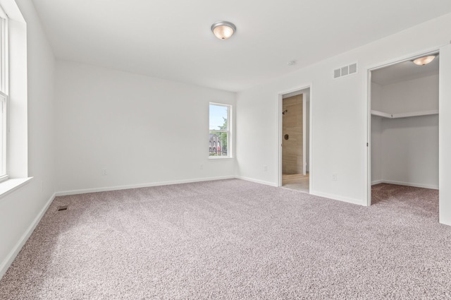 unfurnished bedroom featuring a spacious closet, carpet floors, a closet, and ensuite bathroom