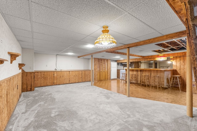 basement with indoor bar, carpet floors, a drop ceiling, and wooden walls