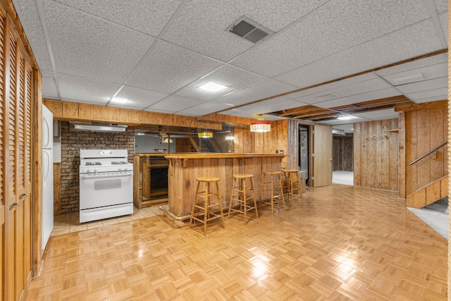 kitchen featuring a breakfast bar, wood walls, white appliances, and kitchen peninsula