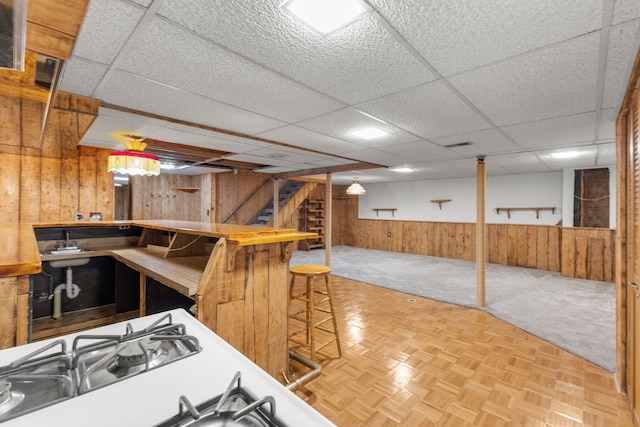 interior space with a paneled ceiling, a breakfast bar, parquet floors, and wood walls