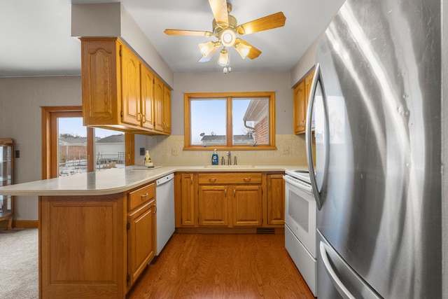 kitchen with tasteful backsplash, sink, white appliances, kitchen peninsula, and light wood-type flooring