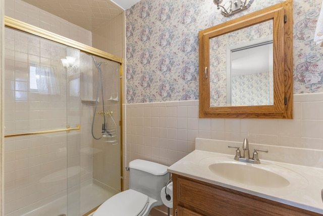 bathroom featuring vanity, toilet, a shower with shower door, and tile walls