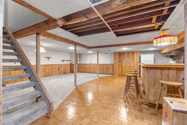 basement featuring wooden walls, white refrigerator, light parquet flooring, and indoor bar