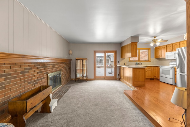 kitchen featuring white appliances, light carpet, light brown cabinets, ceiling fan, and a fireplace