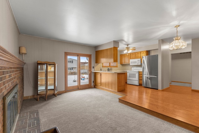 kitchen featuring white appliances, hanging light fixtures, a fireplace, light carpet, and kitchen peninsula