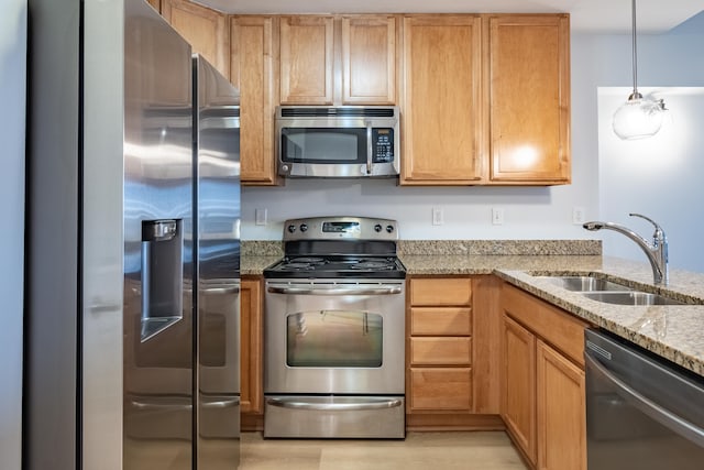 kitchen with appliances with stainless steel finishes, sink, hanging light fixtures, light stone counters, and light hardwood / wood-style floors