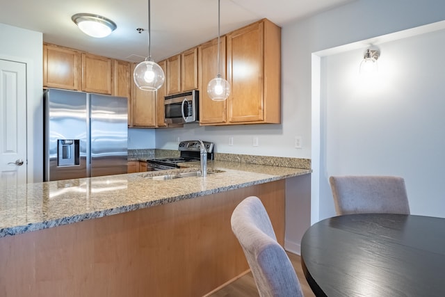 kitchen with sink, appliances with stainless steel finishes, light stone countertops, decorative light fixtures, and kitchen peninsula