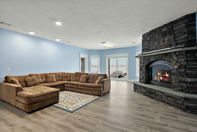 living room featuring a stone fireplace, hardwood / wood-style floors, and a textured ceiling