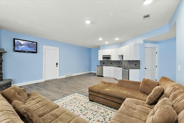 living room with sink, a textured ceiling, and light hardwood / wood-style flooring