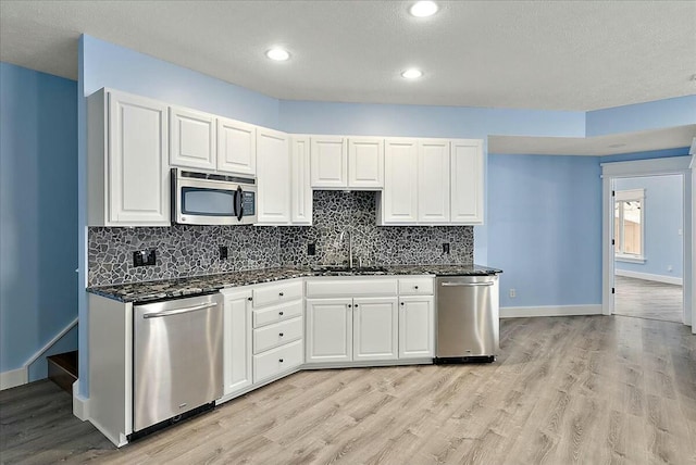 kitchen featuring appliances with stainless steel finishes, sink, white cabinets, dark stone counters, and light hardwood / wood-style floors