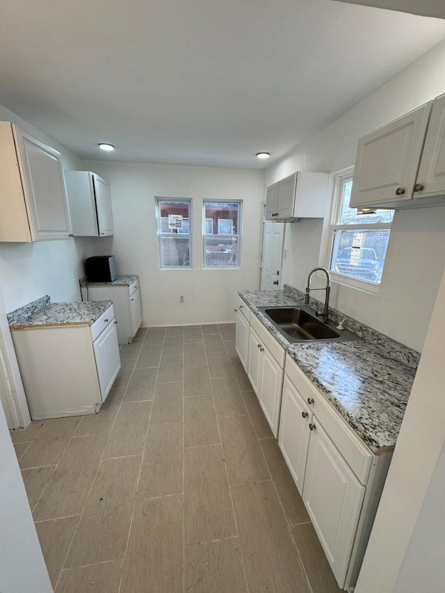 kitchen featuring white cabinetry, sink, and light stone counters