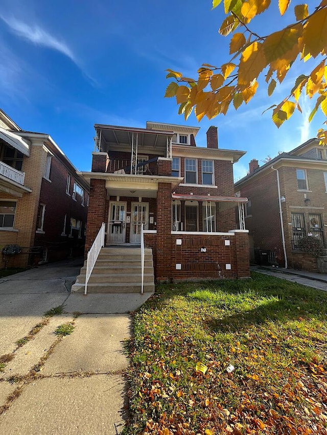 view of front of home with a front yard, french doors, a balcony, and covered porch