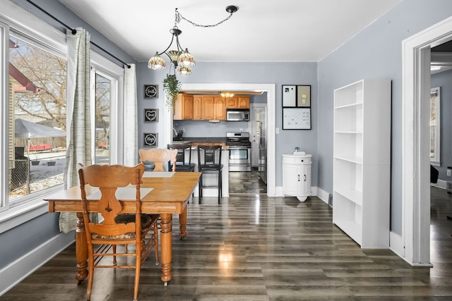 dining space with dark hardwood / wood-style floors, a wealth of natural light, and an inviting chandelier