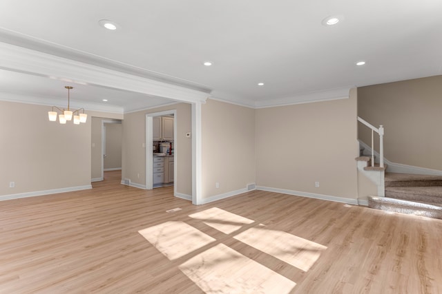 unfurnished living room with crown molding, an inviting chandelier, and light hardwood / wood-style flooring