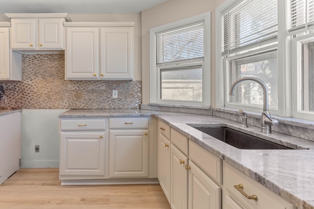 kitchen with sink, tasteful backsplash, white cabinetry, light hardwood / wood-style flooring, and light stone countertops