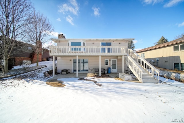 snow covered back of property featuring a wooden deck and a patio area