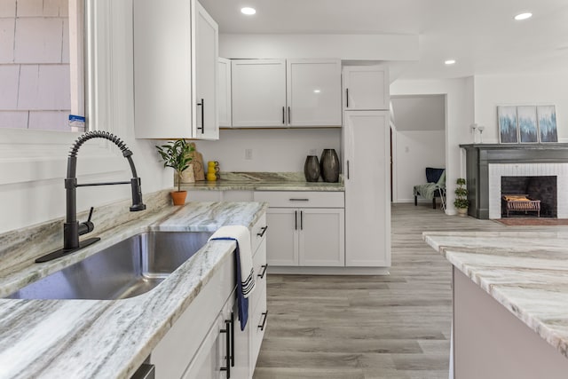 kitchen featuring white cabinetry, sink, light stone countertops, and a brick fireplace