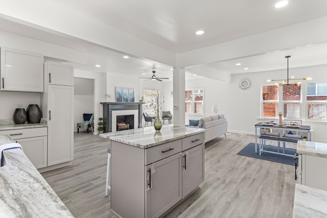 kitchen with pendant lighting, light stone counters, ceiling fan with notable chandelier, and light hardwood / wood-style floors