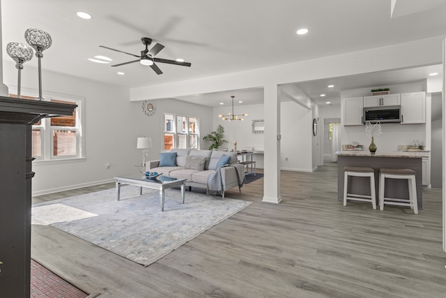 living room featuring ceiling fan with notable chandelier and light wood-type flooring