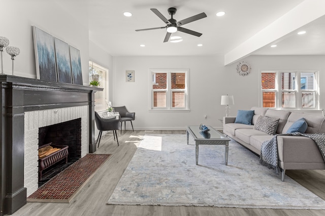 living room with beamed ceiling, ceiling fan, a brick fireplace, and light hardwood / wood-style floors