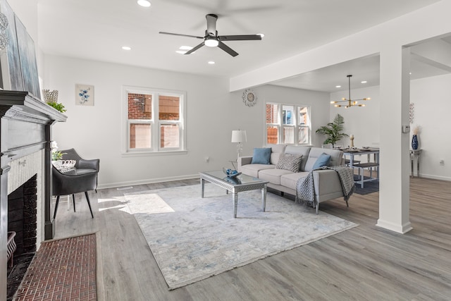 living room with a brick fireplace, ceiling fan with notable chandelier, and light hardwood / wood-style flooring