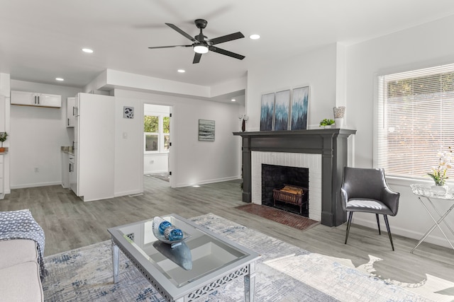 living room with a brick fireplace, ceiling fan, and light wood-type flooring