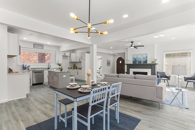 dining space with a brick fireplace, sink, ceiling fan with notable chandelier, and light hardwood / wood-style flooring