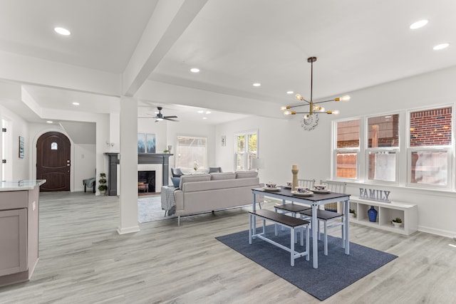 dining room with a fireplace, beam ceiling, ceiling fan with notable chandelier, and light wood-type flooring