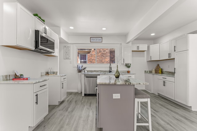 kitchen featuring a kitchen island, appliances with stainless steel finishes, white cabinetry, a kitchen bar, and light hardwood / wood-style flooring