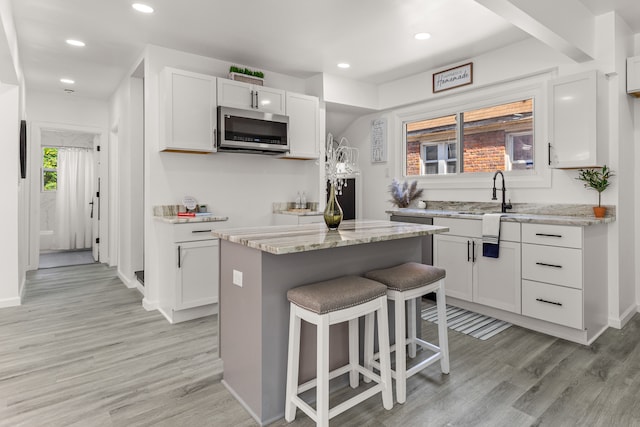 kitchen featuring white cabinetry, sink, a center island, light stone counters, and light wood-type flooring