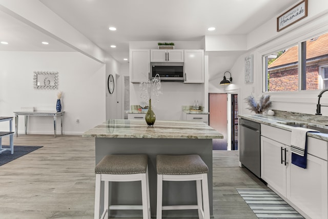 kitchen with sink, a breakfast bar, white cabinetry, stainless steel appliances, and light stone countertops