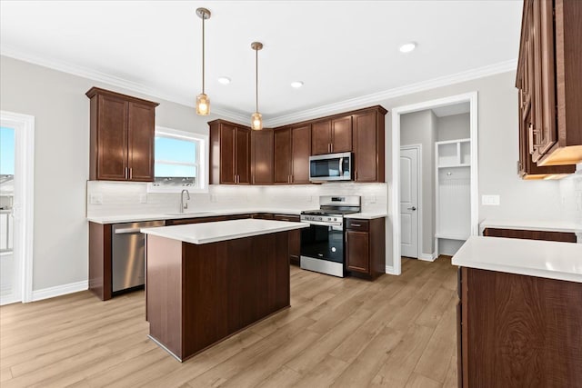 kitchen featuring sink, crown molding, appliances with stainless steel finishes, a kitchen island, and decorative light fixtures