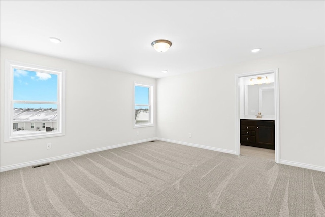 unfurnished bedroom featuring multiple windows, ensuite bathroom, and light carpet