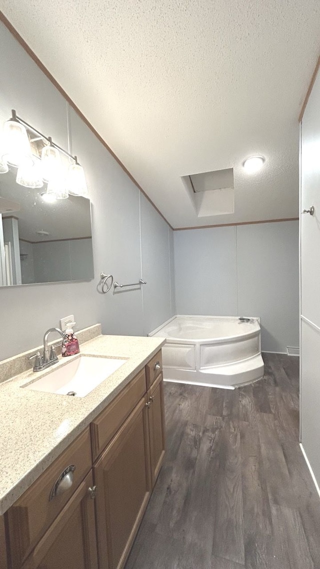 bathroom featuring hardwood / wood-style floors, vaulted ceiling, vanity, a textured ceiling, and a bathing tub