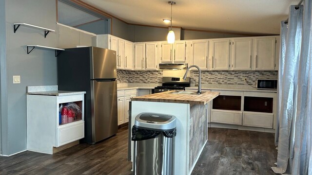 kitchen with wooden counters, vaulted ceiling, a center island with sink, stainless steel appliances, and white cabinets