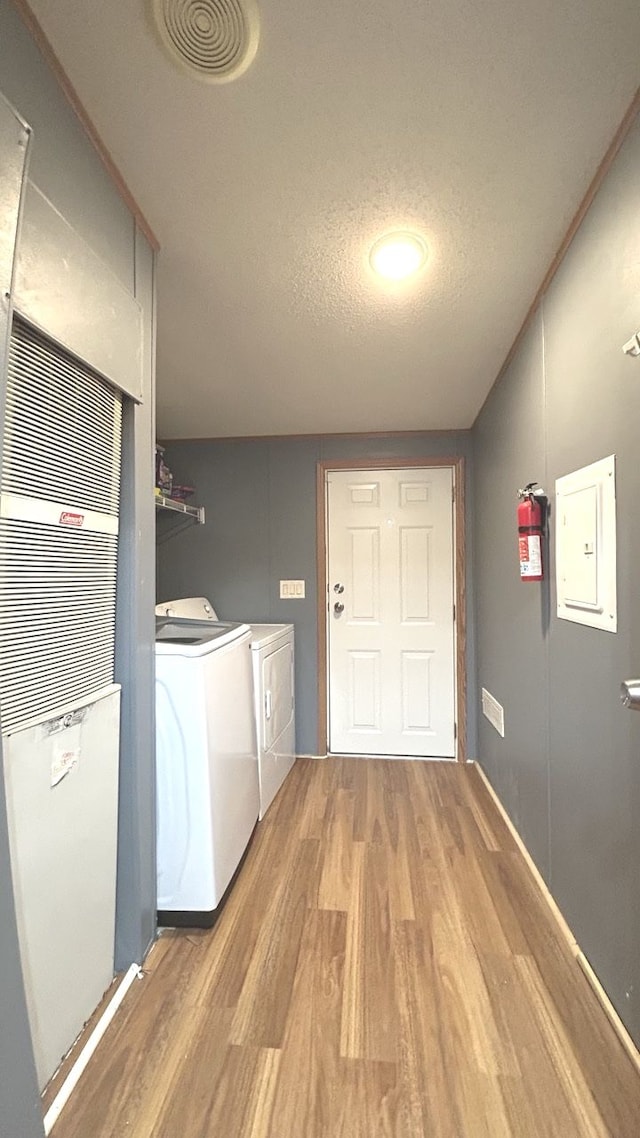 laundry area featuring electric panel, light hardwood / wood-style flooring, washer and dryer, and a textured ceiling