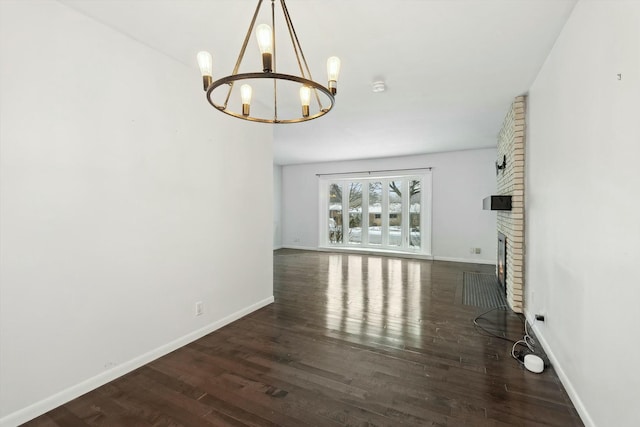 unfurnished living room with a brick fireplace, dark hardwood / wood-style floors, and a notable chandelier