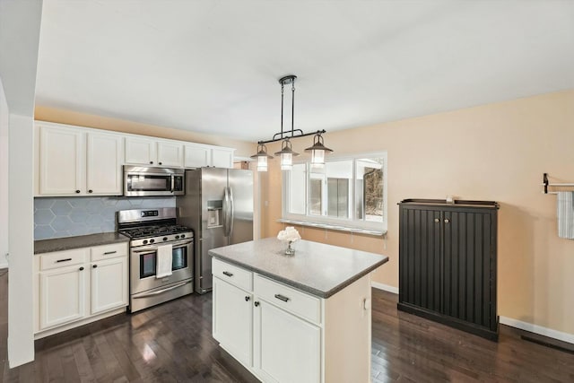 kitchen with appliances with stainless steel finishes, decorative light fixtures, white cabinets, backsplash, and a center island